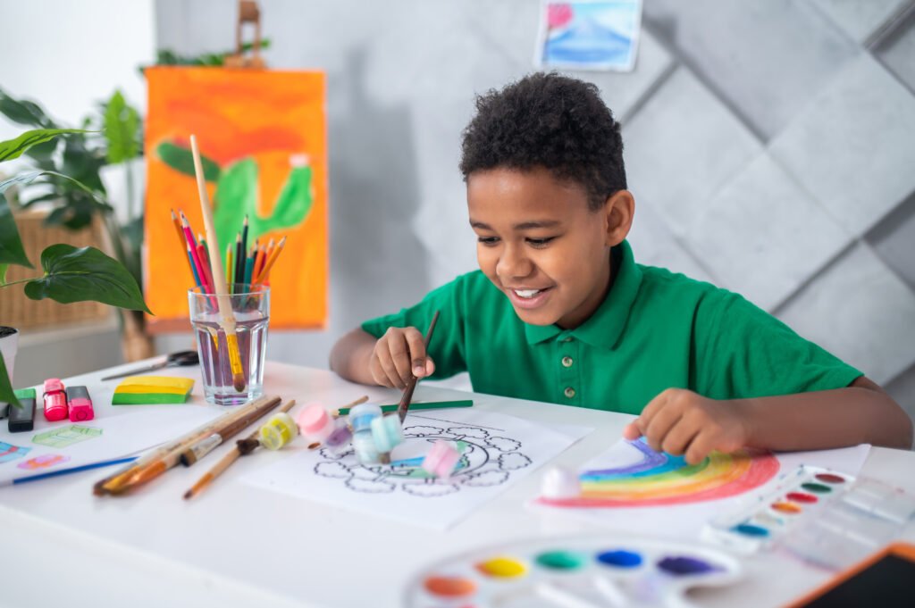 boy sitting at table pushing tubes of paint